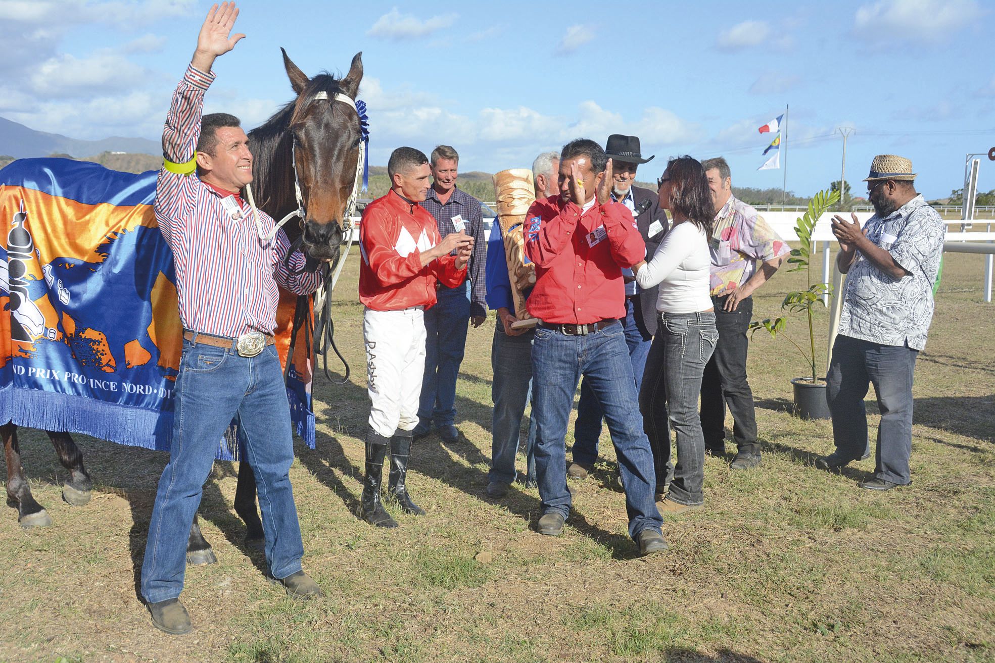 Le hongre Reia de Tamoa, avec son jockey sud-africain Devin Ashby (casque rouge et pantalon blanc) et son  entraîneur Patrick Greppo (chemise rouge, jean foncé).